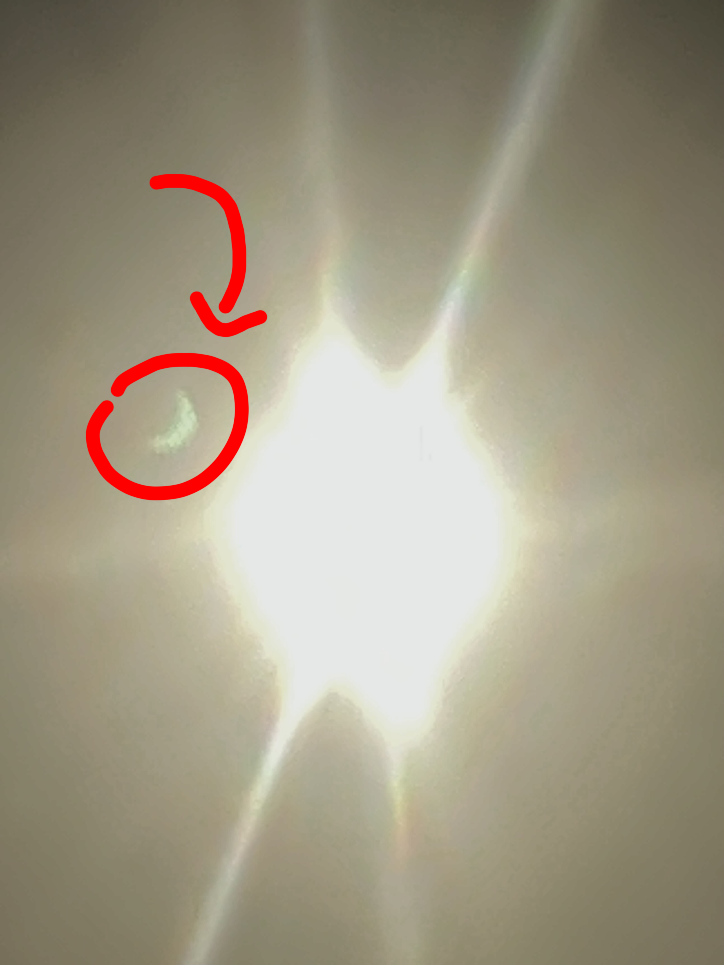 a badly overexposed sun blown out into a starburst, with a tiny separate green crescent elsewhere in the frame -- a lens ghost